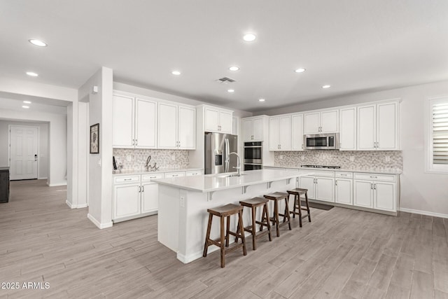 kitchen with light hardwood / wood-style flooring, a kitchen breakfast bar, an island with sink, stainless steel appliances, and white cabinets