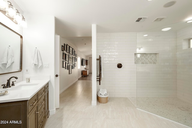 bathroom with tile patterned flooring, a tile shower, and vanity