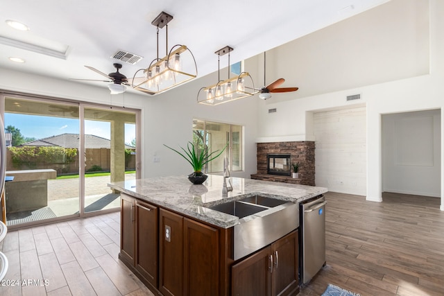 kitchen featuring a center island with sink, light stone counters, stainless steel dishwasher, wood-type flooring, and pendant lighting