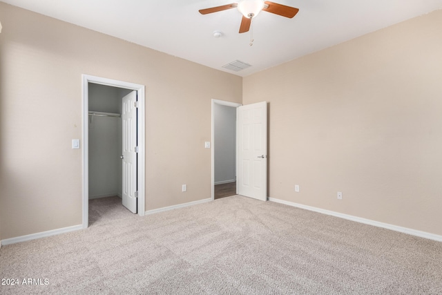 unfurnished bedroom with light colored carpet, ceiling fan, a walk in closet, and a closet