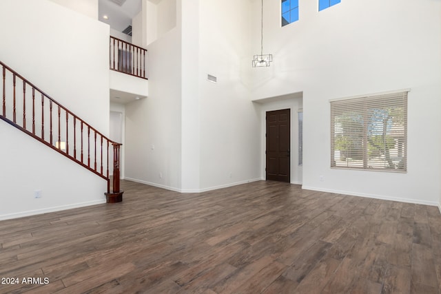 unfurnished living room with a high ceiling, an inviting chandelier, and dark hardwood / wood-style floors