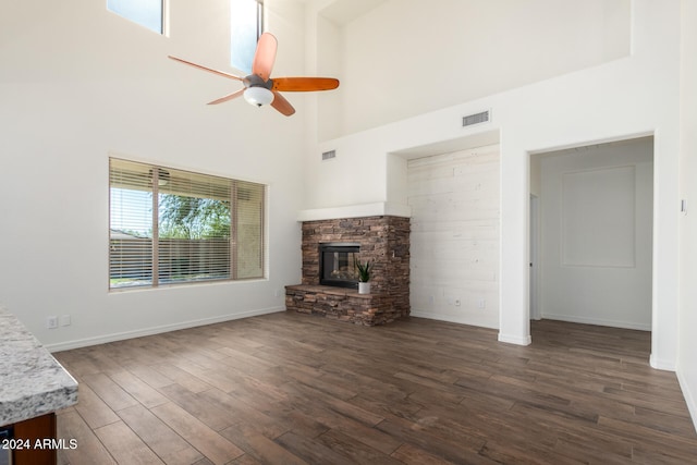 unfurnished living room with a fireplace, a high ceiling, ceiling fan, and dark hardwood / wood-style flooring