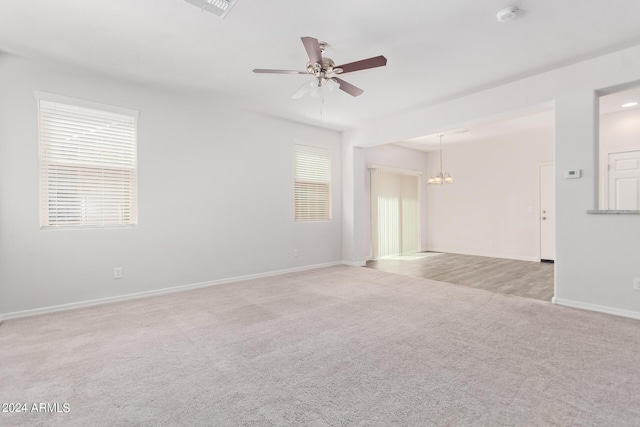 carpeted empty room with plenty of natural light, visible vents, baseboards, and ceiling fan with notable chandelier