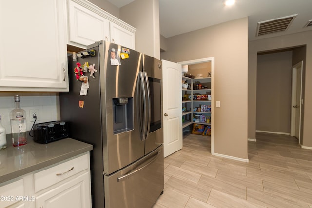 kitchen featuring backsplash, stainless steel fridge, and white cabinets