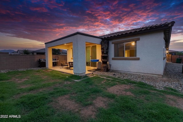 back house at dusk with a patio area and a yard