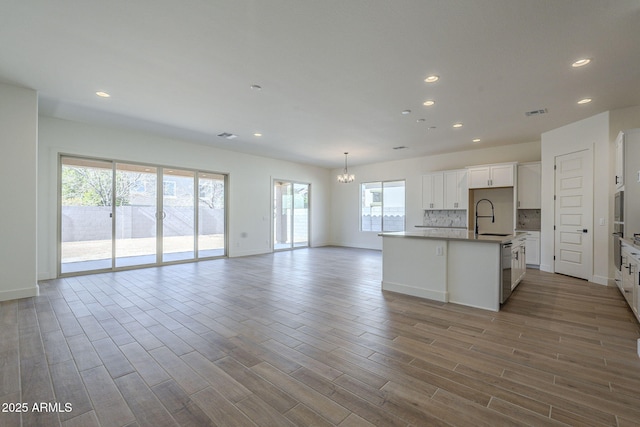 kitchen with sink, light hardwood / wood-style flooring, white cabinetry, an island with sink, and decorative backsplash