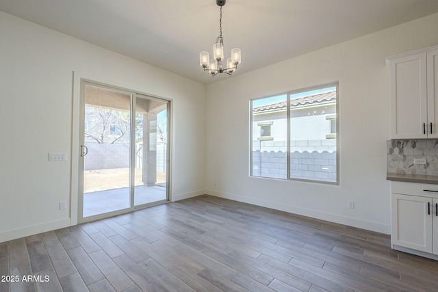 unfurnished dining area with an inviting chandelier, a wealth of natural light, and light hardwood / wood-style floors