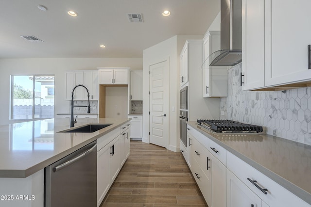 kitchen with white cabinetry, appliances with stainless steel finishes, sink, and wall chimney range hood