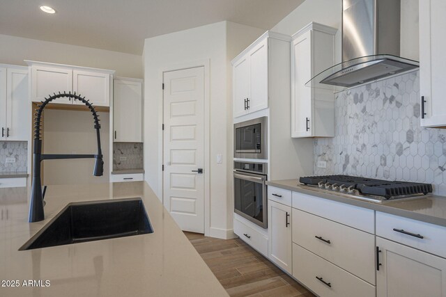 kitchen featuring sink, white cabinets, wall chimney exhaust hood, and appliances with stainless steel finishes