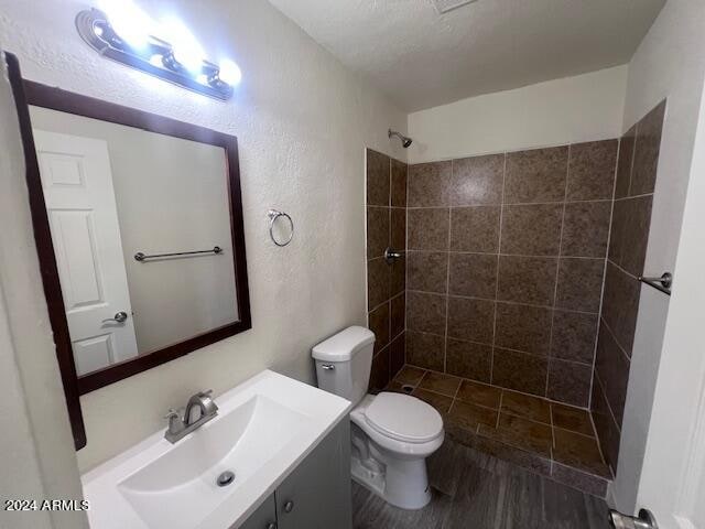 bathroom with hardwood / wood-style flooring, a tile shower, vanity, and toilet