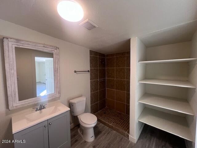 bathroom with hardwood / wood-style floors, vanity, tiled shower, and toilet