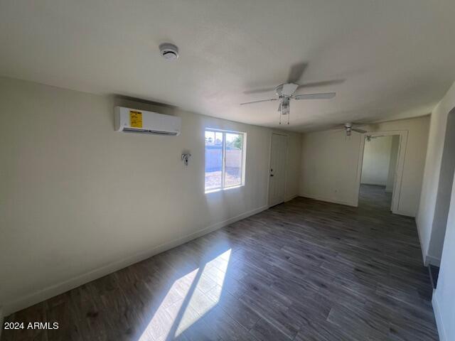 empty room featuring ceiling fan, dark hardwood / wood-style floors, and an AC wall unit