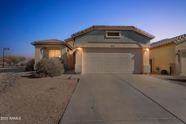 view of front of house featuring a garage, driveway, a tiled roof, and stucco siding