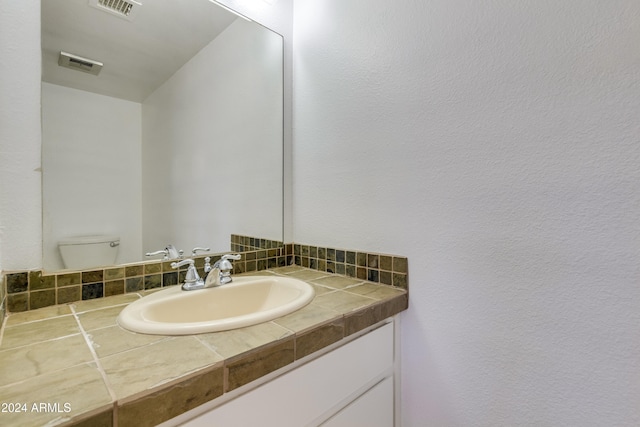 bathroom featuring vanity, toilet, and tasteful backsplash