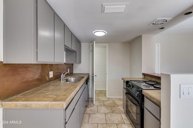 kitchen featuring black range with electric cooktop, sink, stainless steel dishwasher, tile counters, and gray cabinets