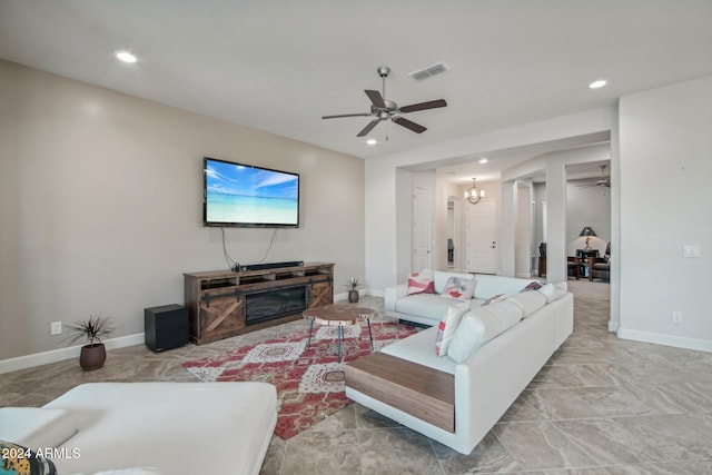 living room with ceiling fan with notable chandelier and a stone fireplace