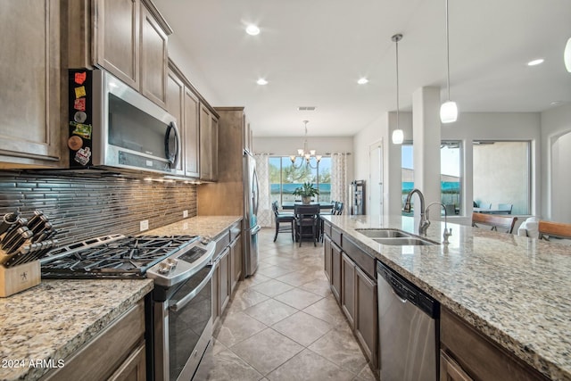 kitchen with light stone countertops, appliances with stainless steel finishes, sink, decorative light fixtures, and a notable chandelier