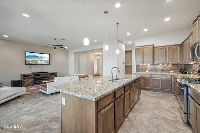 kitchen with pendant lighting, a kitchen island with sink, sink, ceiling fan, and appliances with stainless steel finishes