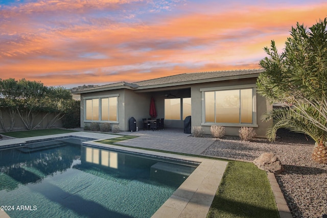 back house at dusk featuring a patio area and a fenced in pool