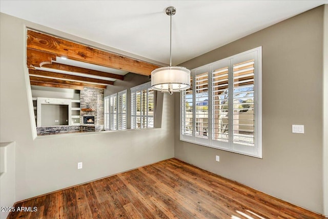 unfurnished dining area featuring an inviting chandelier, a stone fireplace, wood-type flooring, and beamed ceiling