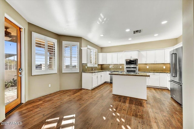 kitchen with appliances with stainless steel finishes, tasteful backsplash, white cabinets, dark stone counters, and a center island