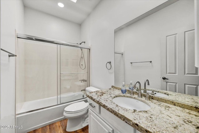 full bathroom with hardwood / wood-style flooring, vanity, bath / shower combo with glass door, and toilet