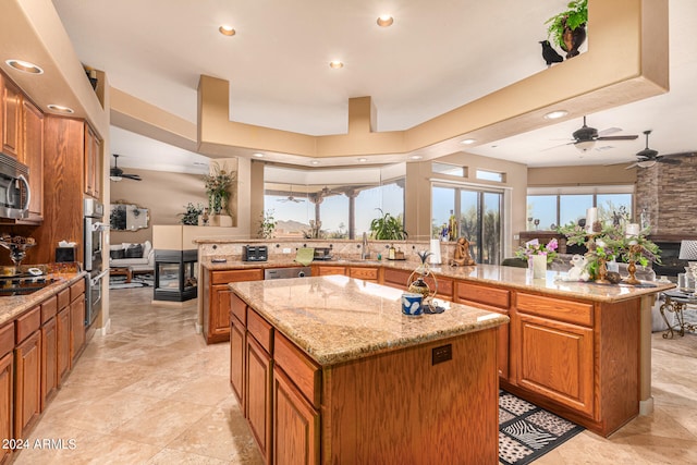 kitchen featuring light stone counters, ceiling fan, a center island, light tile floors, and stainless steel appliances