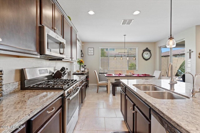 kitchen featuring pendant lighting, dark brown cabinets, sink, stainless steel appliances, and light stone countertops