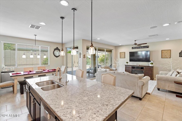 kitchen with decorative light fixtures, sink, light stone counters, and a kitchen island with sink