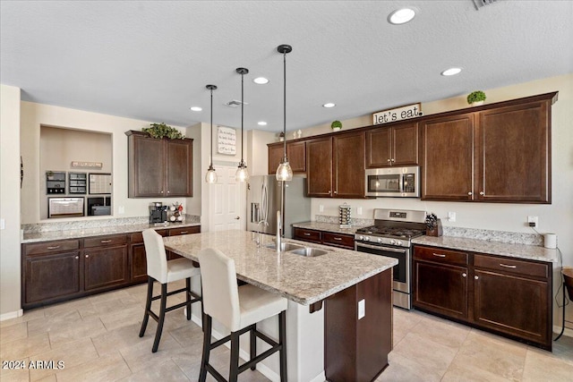 kitchen with a breakfast bar, a center island with sink, decorative light fixtures, sink, and appliances with stainless steel finishes