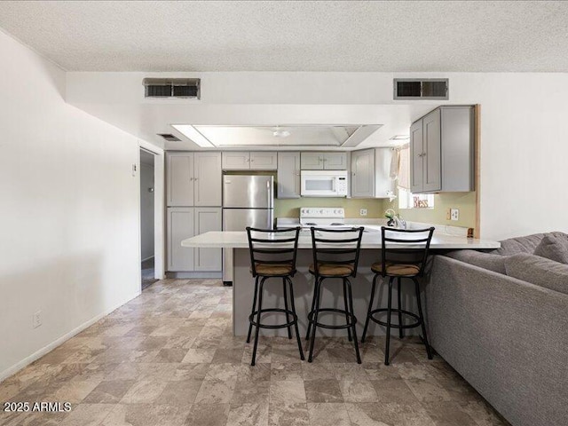kitchen featuring white appliances, a peninsula, visible vents, and gray cabinets