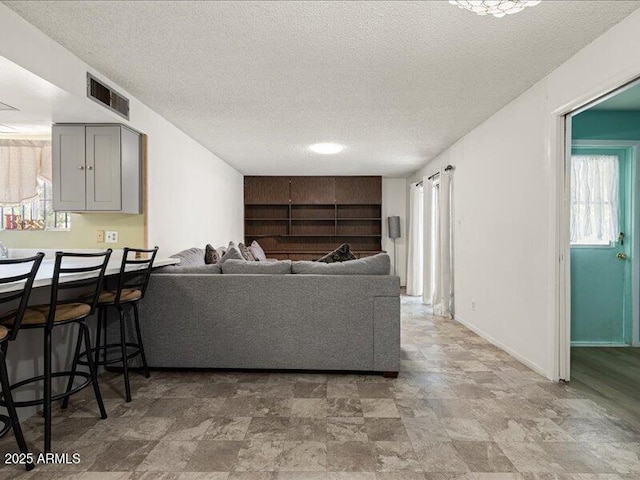 living room featuring a textured ceiling, a wealth of natural light, stone finish floor, and visible vents
