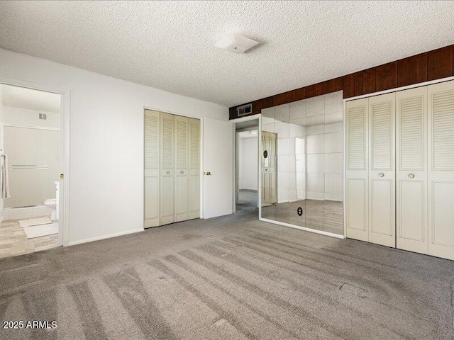 unfurnished bedroom featuring carpet flooring, visible vents, two closets, and a textured ceiling