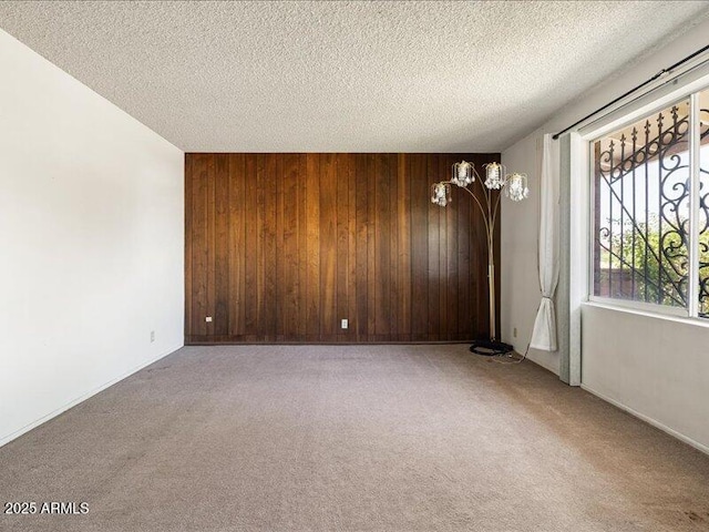 spare room with carpet flooring, a textured ceiling, wood walls, and baseboards