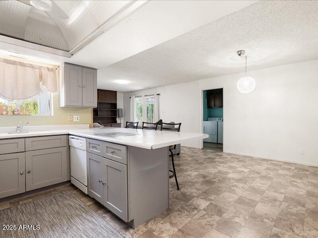 kitchen featuring washer and dryer, a peninsula, a sink, gray cabinets, and dishwasher