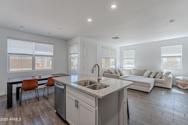 kitchen with visible vents, open floor plan, a kitchen island with sink, a sink, and white cabinetry