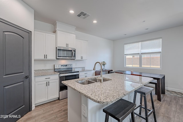 kitchen featuring visible vents, stainless steel appliances, a sink, and a center island with sink