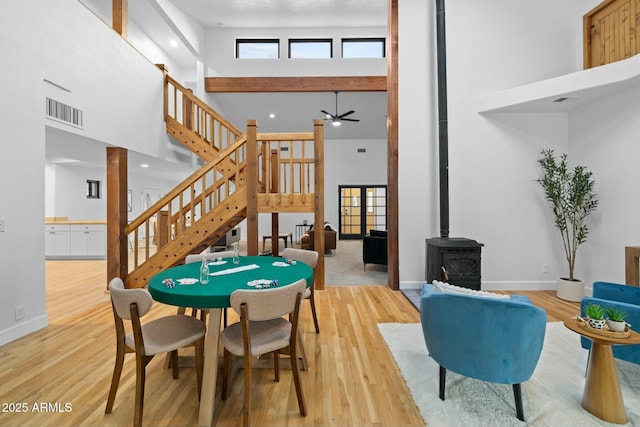 rec room with light wood finished floors, visible vents, a high ceiling, a wood stove, and baseboards