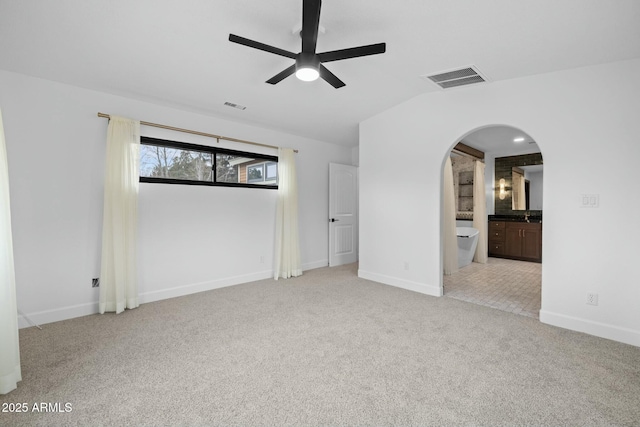 empty room featuring arched walkways, vaulted ceiling, carpet, and visible vents