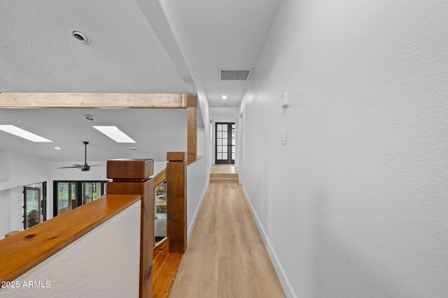 corridor with light wood-style flooring, a skylight, visible vents, and baseboards