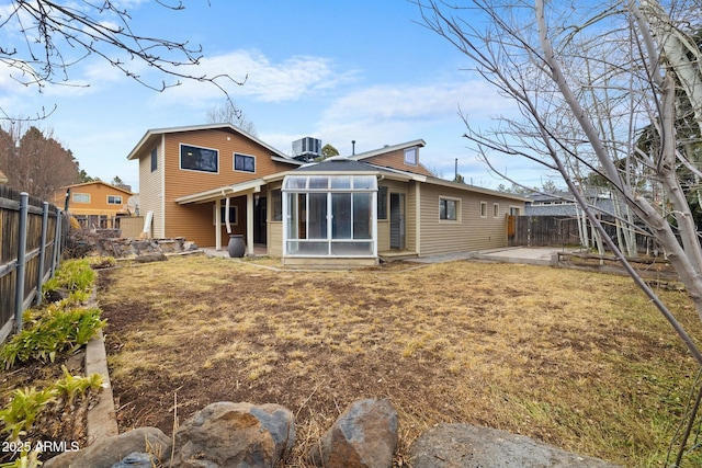 rear view of house with a lawn, a patio, a sunroom, a fenced backyard, and central AC