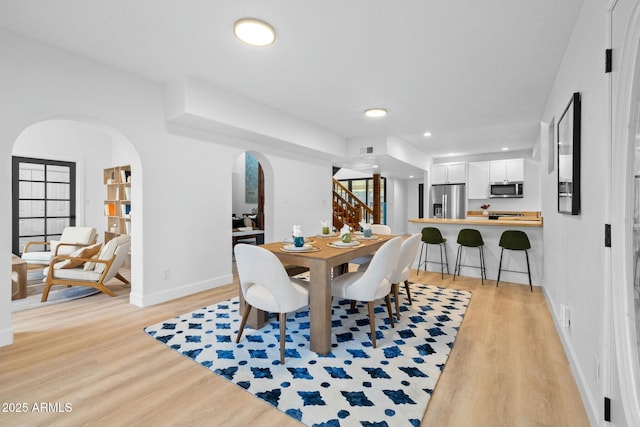 dining room with light wood finished floors, baseboards, stairway, and arched walkways