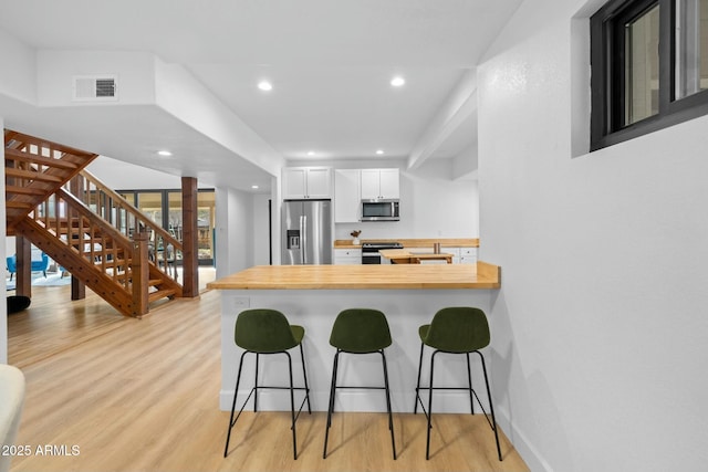 kitchen featuring butcher block counters, appliances with stainless steel finishes, light wood-type flooring, a peninsula, and a kitchen breakfast bar