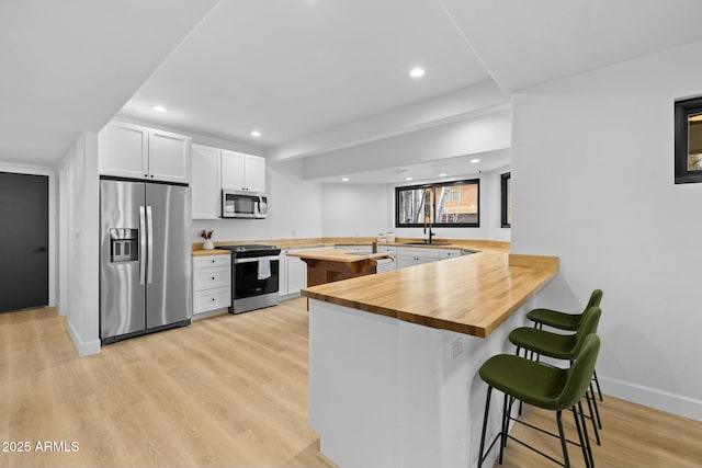 kitchen with stainless steel appliances, a breakfast bar, a peninsula, wooden counters, and light wood finished floors