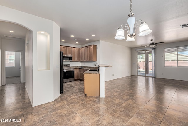 kitchen featuring pendant lighting, stone counters, ceiling fan with notable chandelier, kitchen peninsula, and stainless steel appliances