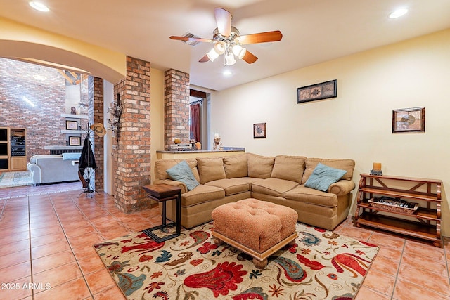 tiled living room with ceiling fan and brick wall