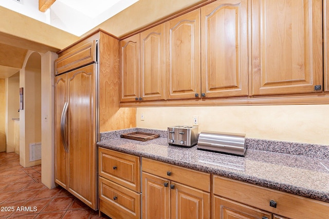 kitchen with tile patterned floors, dark stone counters, and paneled fridge