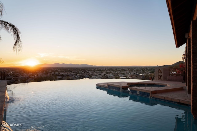 pool at dusk featuring a water view and an in ground hot tub