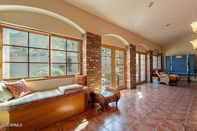 living area featuring lofted ceiling, plenty of natural light, tile patterned floors, and ornate columns