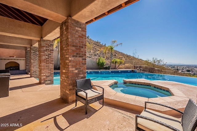 view of pool featuring an in ground hot tub, exterior fireplace, a mountain view, and a patio area